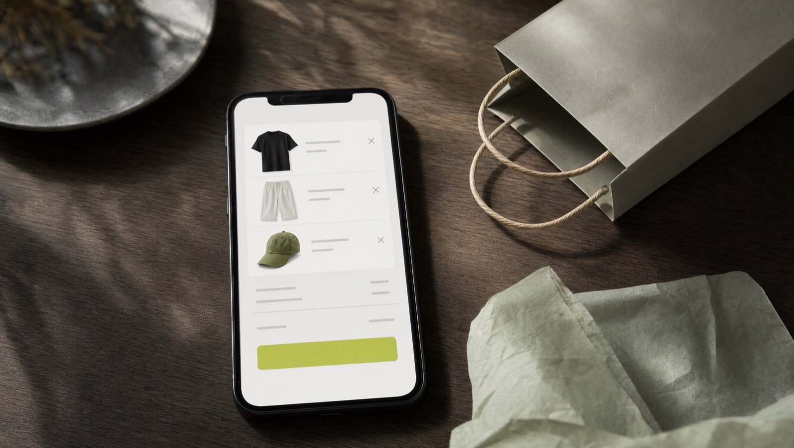 Smartphone showing an online clothing store cart beside a tipped-over paper shopping bag